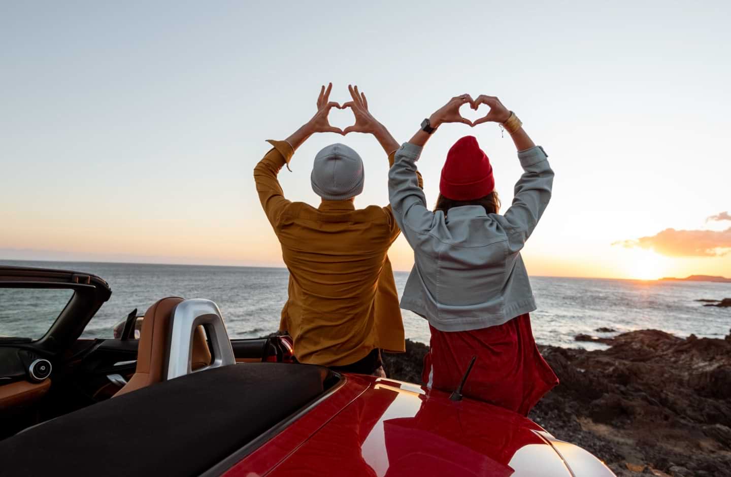 Duas pessoas fazem corações com as mãos a ver um pôr do sol